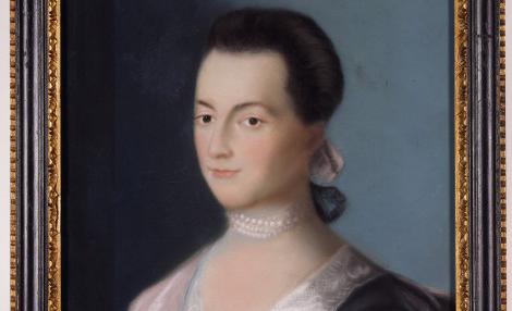 A framed portrait of a young woman with dark hair. She wears a blue dress with lace around the neckline, 粉红色的包装纸, a pearl choker necklace, and a pink ribbon in her hair.